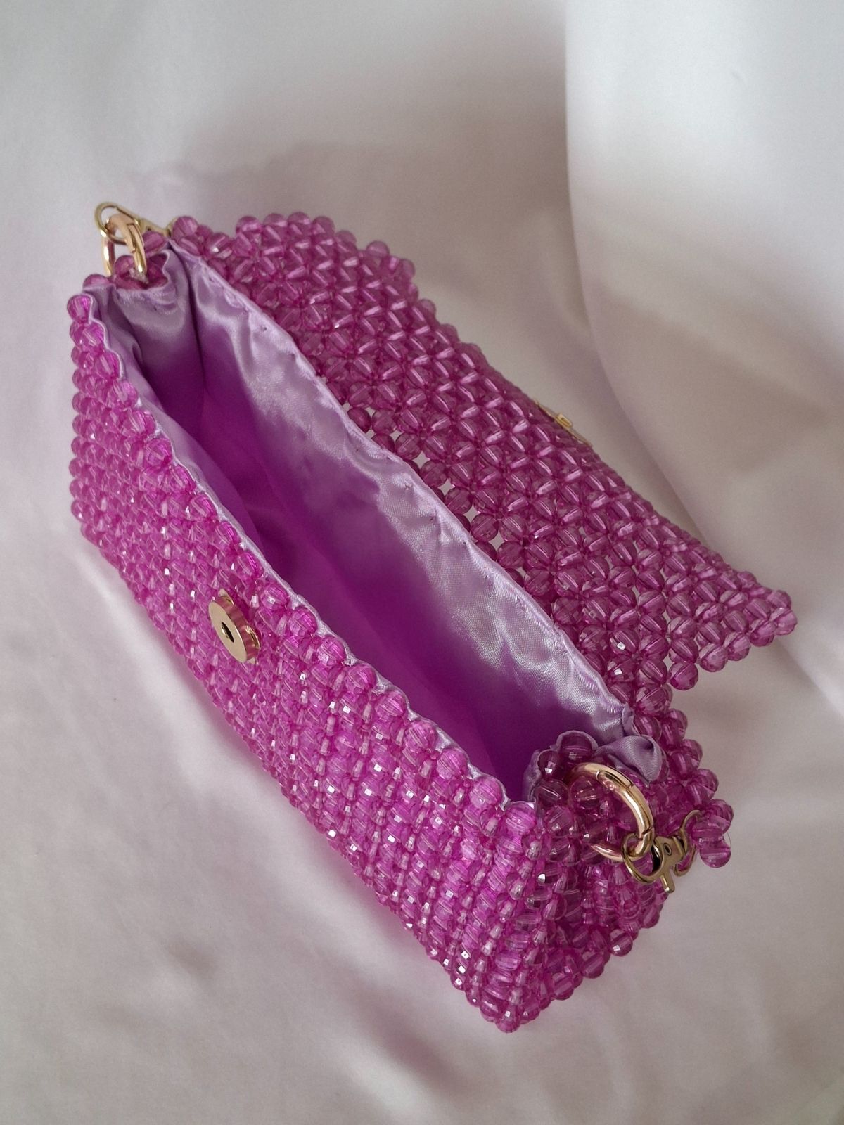 Pink beaded handbag with gold accents on a white background