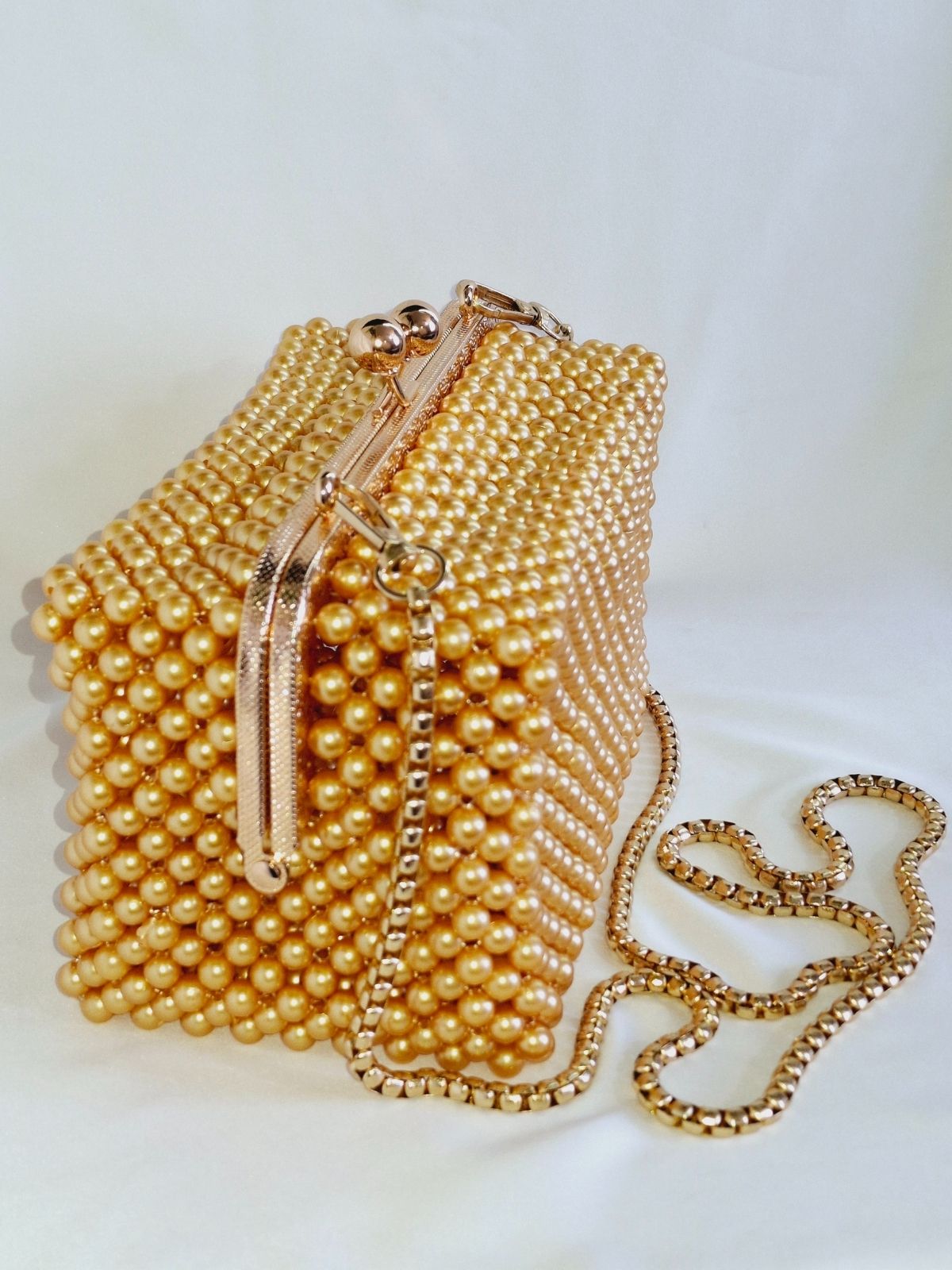 Gold pearl-handled handbag with chain strap on a light background