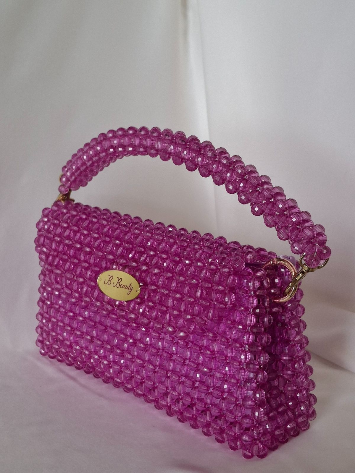 Pink beaded handbag with a visible brand logo on a white background