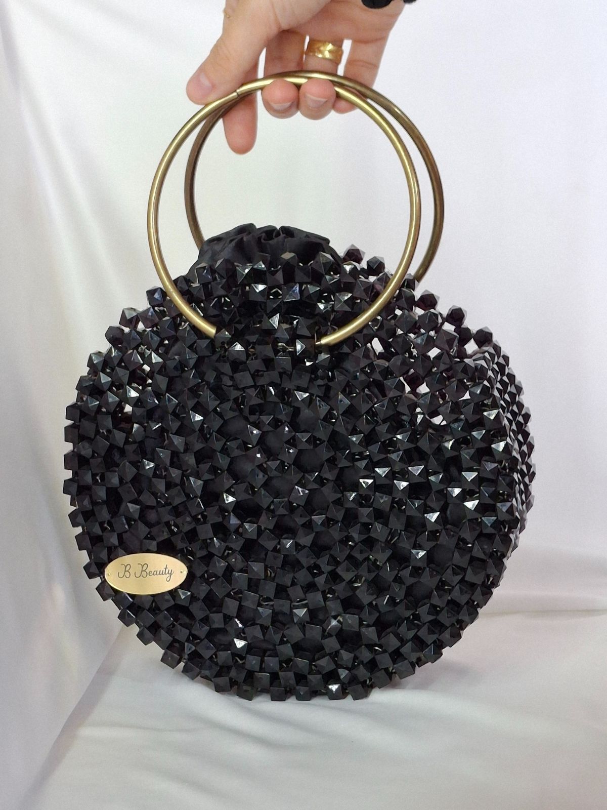 Black beaded handbag with gold handle held by a hand on a white background