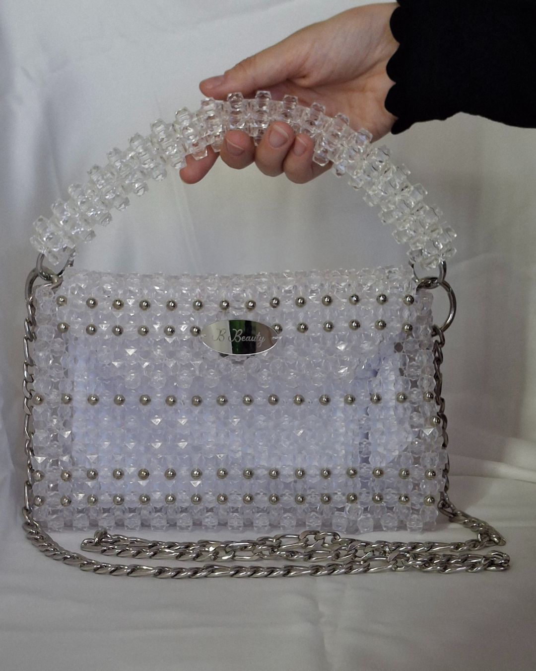 Handbag with clear handle and silver studs held by a hand against a white background